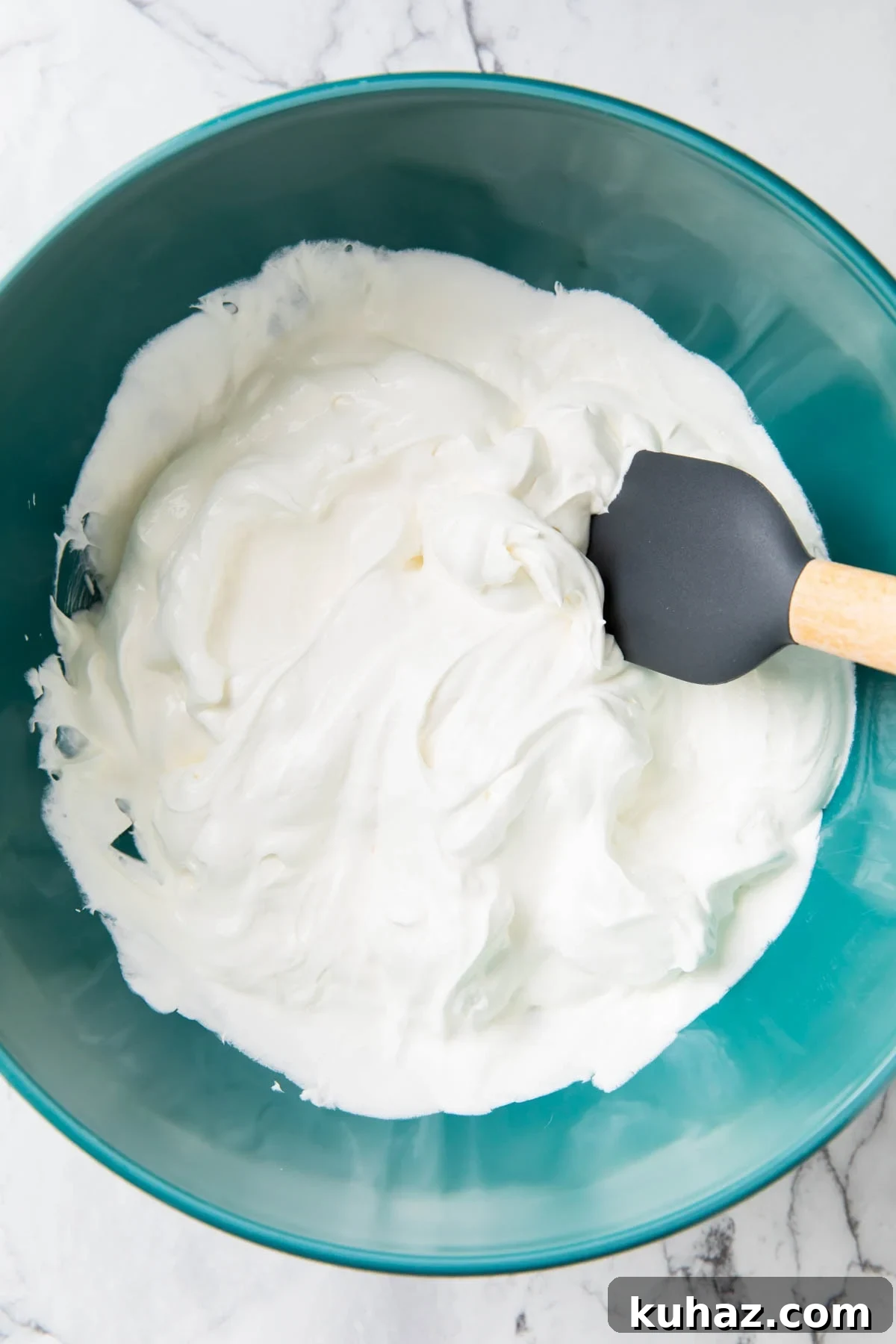 A photo showing how to make Ambrosia Salad - Folding Cool Whip frozen whipped topping and vanilla yogurt together to make creamy fruit salad dressing.
