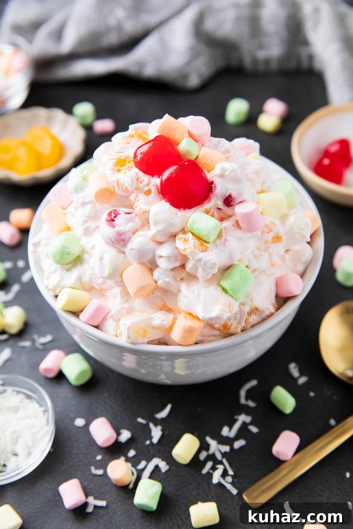 Ambrosia watergate salad is served with lots of marshmallows, topped with maraschino cherries, and extra fruit topping.