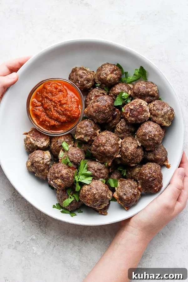 Oven Baked Meatballs A bowl of cooked meatballs with a small bowl of marinara sauce and some fresh parsley on top.