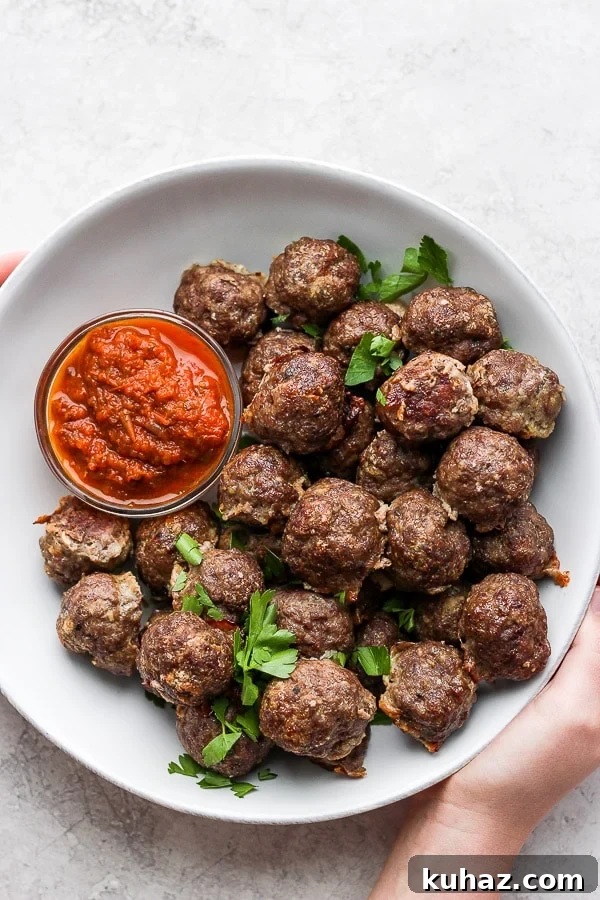 Oven Baked Meatballs Served with Sauce Oven baked meatballs in a large white bowl with a small dish of marinara sauce.