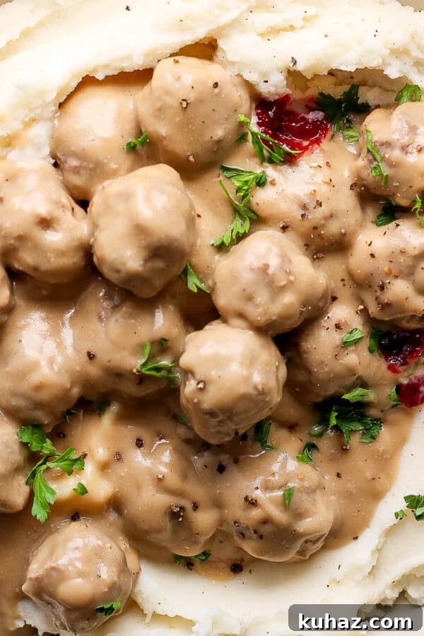 Juicy Oven Baked Meatballs Recipe 3 Top down shot of a big bowl of mashed potatoes topped with swedish meatballs, parsley, lingonberry jam and cracked pepper.