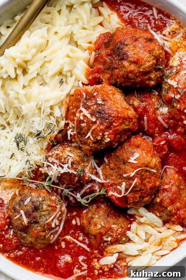 Juicy Oven Baked Meatballs Recipe 5 Bowl of Italian Meatballs in red sauce with parmesan orzo and fresh oregano leaves on top.