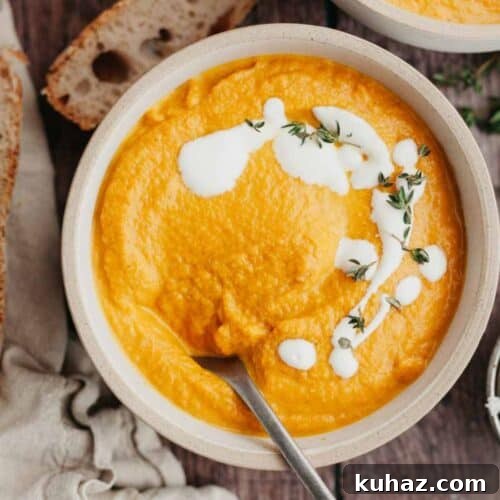 A white bowl with pumpkin carrot soup in it, drizzled with heavy cream and thyme.