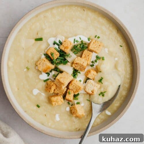 A bowl of cauliflower leek and potato soup with croutons and chopped dill.