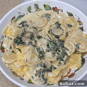 Lobster and Spinach Ravioli in Creamy Garlic Sauce 4 A bowl of Creamy Spinach Lobster Ravioli covered in a luscious white sauce with spinach and small slices of onion, served on a decorative plate.