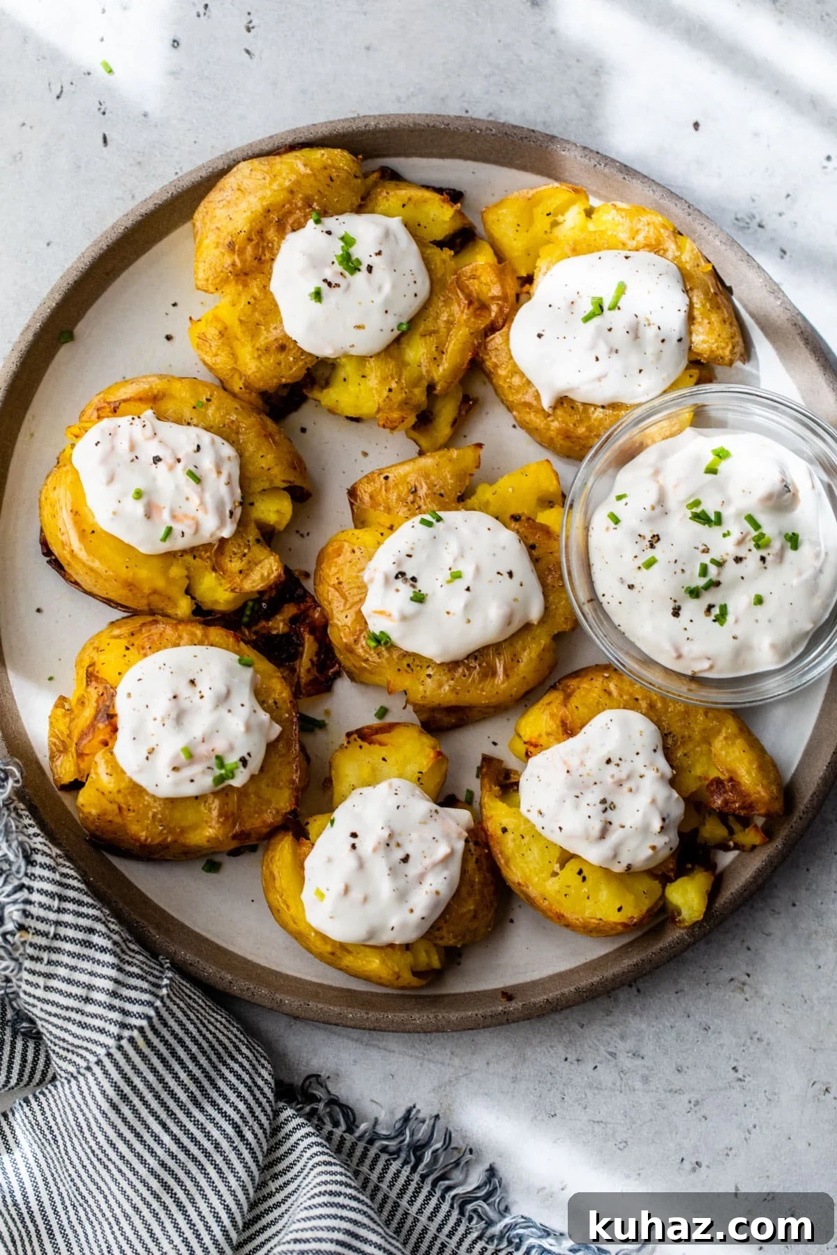 Crispy Smashed Potatoes with Sour Cream Recipe 5 crispy smashed potatoes on a plate with dollops of garlic cheddar sour cream on top