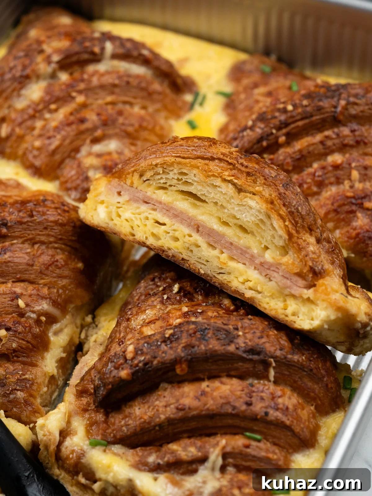 Make-Ahead Ham and Cheese Croissant Breakfast Casserole 2 Cross section of croissant breakfast casserole showing flaky croissant, ham, melted cheese and egg. milk layer.