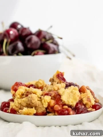 Chewy 4-Ingredient Brownie Mix Cookies 15 cherry dump cake on a white plate with a bowl of cherries behind