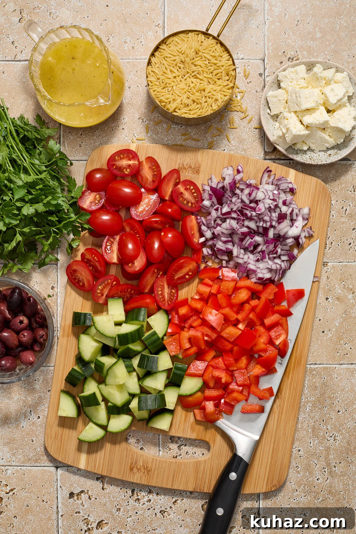 Chopped vegetables on a wooden board with remaining salad ingredients surrounding it.