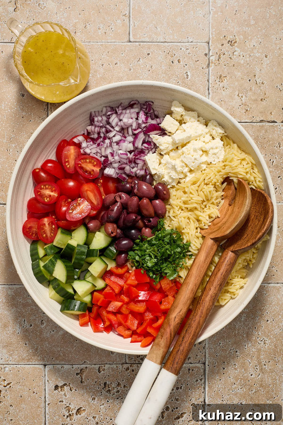 Salad ingredients sectioned in a white bowl with salad servers and dressing on the side.