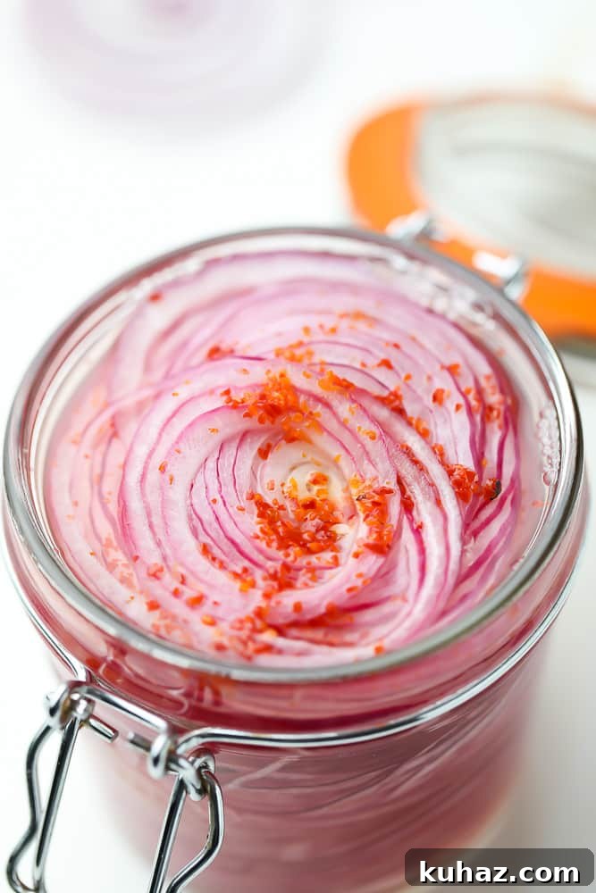 Pickled Red Onions Recipe for Tacos, Salads and Sandwiches 4 close up of sliced red onions in a mason jar with red flakes on top