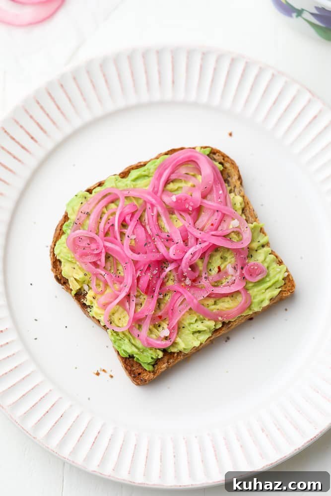 Pickled Red Onions Recipe for Tacos, Salads and Sandwiches 6 slices of pickled red onions on a piece of avocado toast on a white plate