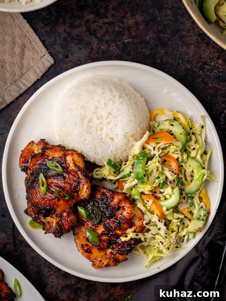 white plate with mound of white rice, two chicken thighs and serving of Asian cucumber slaw