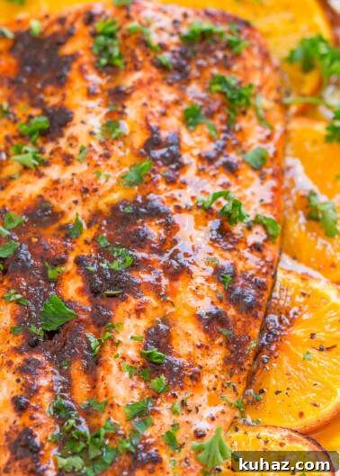 Oven-baked salmon fillet with a glaze, garnished with slices of orange and parsley.