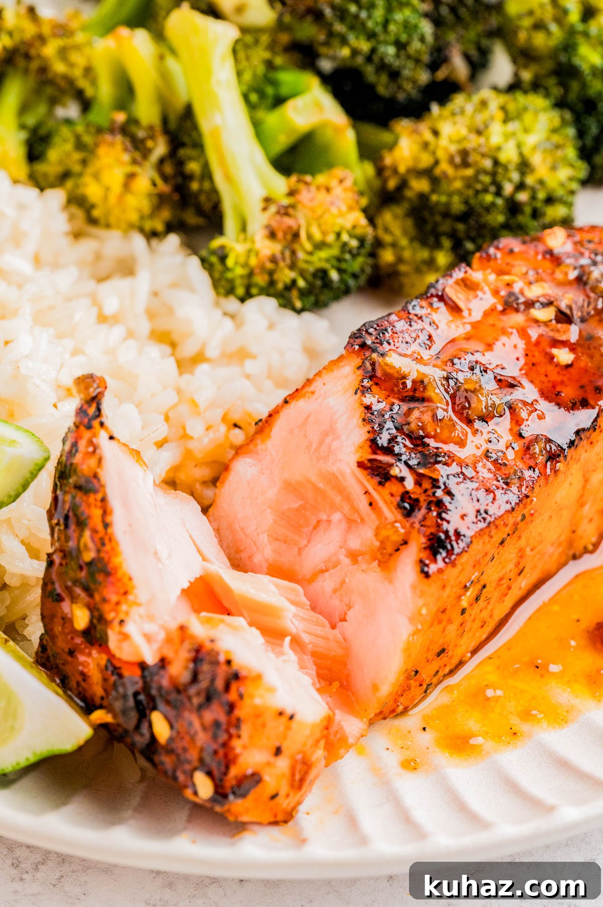 A plate with grilled salmon, white rice, broccoli, and a lime wedge. The salmon is partially cut to show its tender, flaky interior.