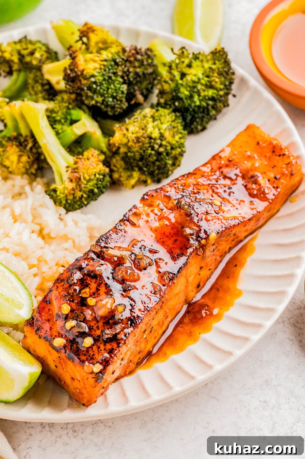 A plate with a glazed salmon fillet, steamed broccoli, white rice, and lime wedges.