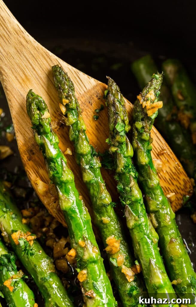 Garlic Sautéed Asparagus Recipe 2 Four sautéed asparagus spears held up on a wooden spatula in a pan.