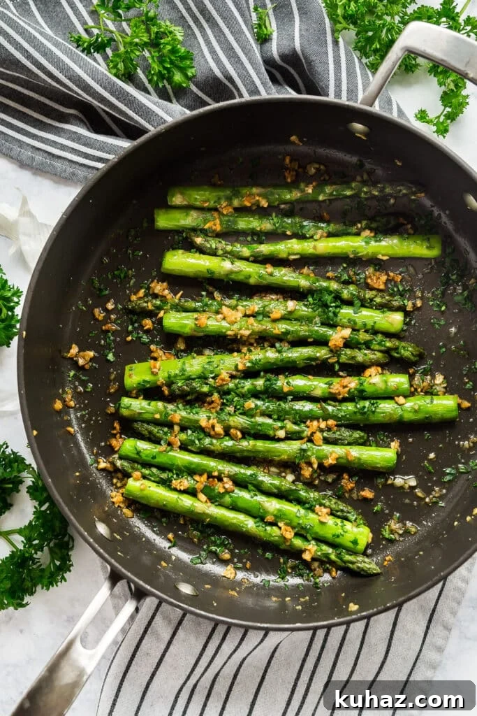 Garlic Sautéed Asparagus Recipe 3 An overhead image of a black sauté pan with perfectly pan seared asparagus with garlic and parsley around it.
