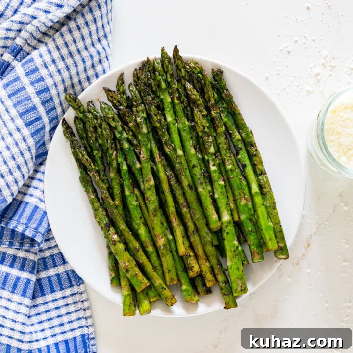 An overhead image of a plate of asparagus with a blue and white towel and Romano cheese around it.