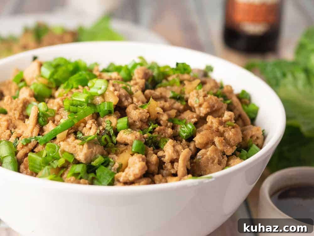 Instant Pot Chicken Lettuce Wraps: Copycat Takeout Recipe 3 Side view of Instant Pot chicken lettuce wraps filling in a white bowl, garnished with green onions, with lettuce and sauce on a wooden table.