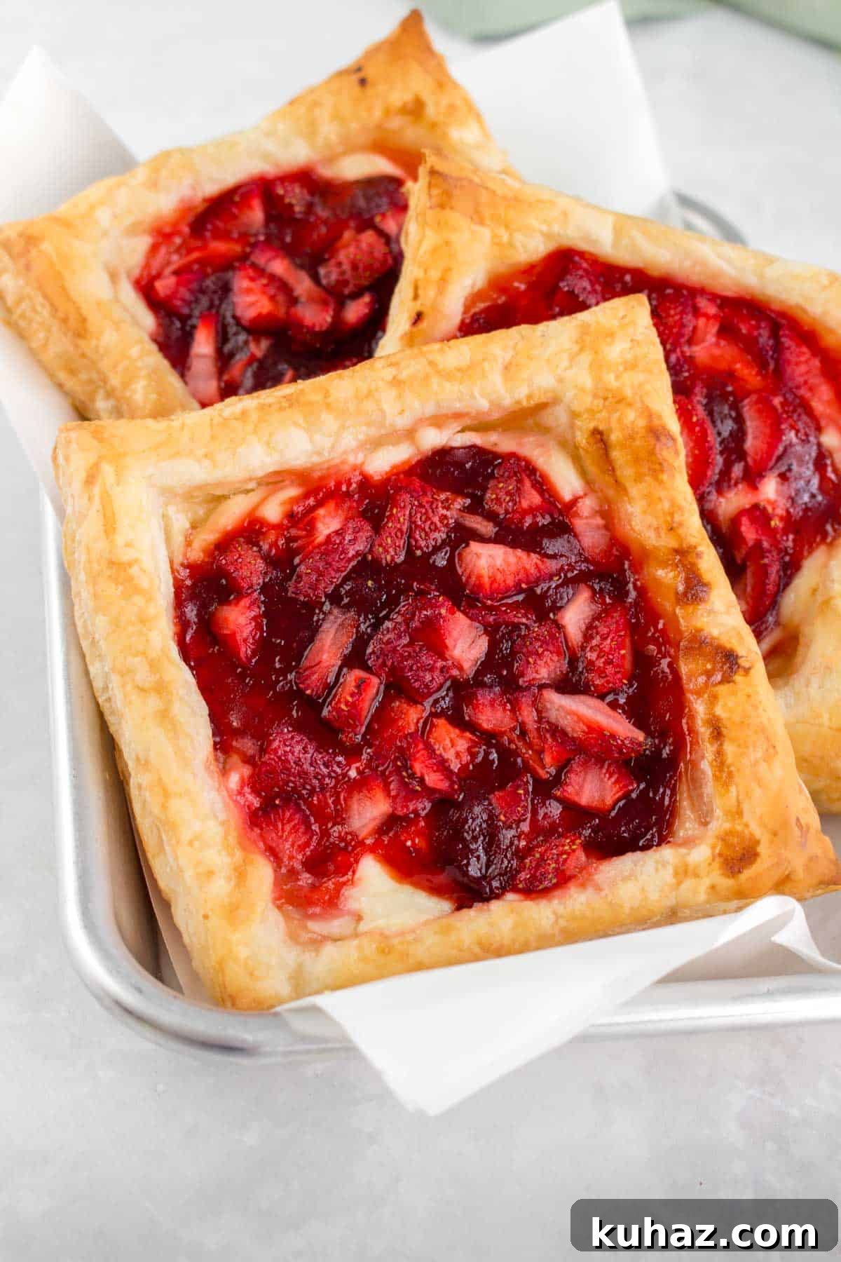 Flaky Homemade Strawberry Danish with Cream Cheese Recipe 11 Three strawberry danishes on a small sheet pan.