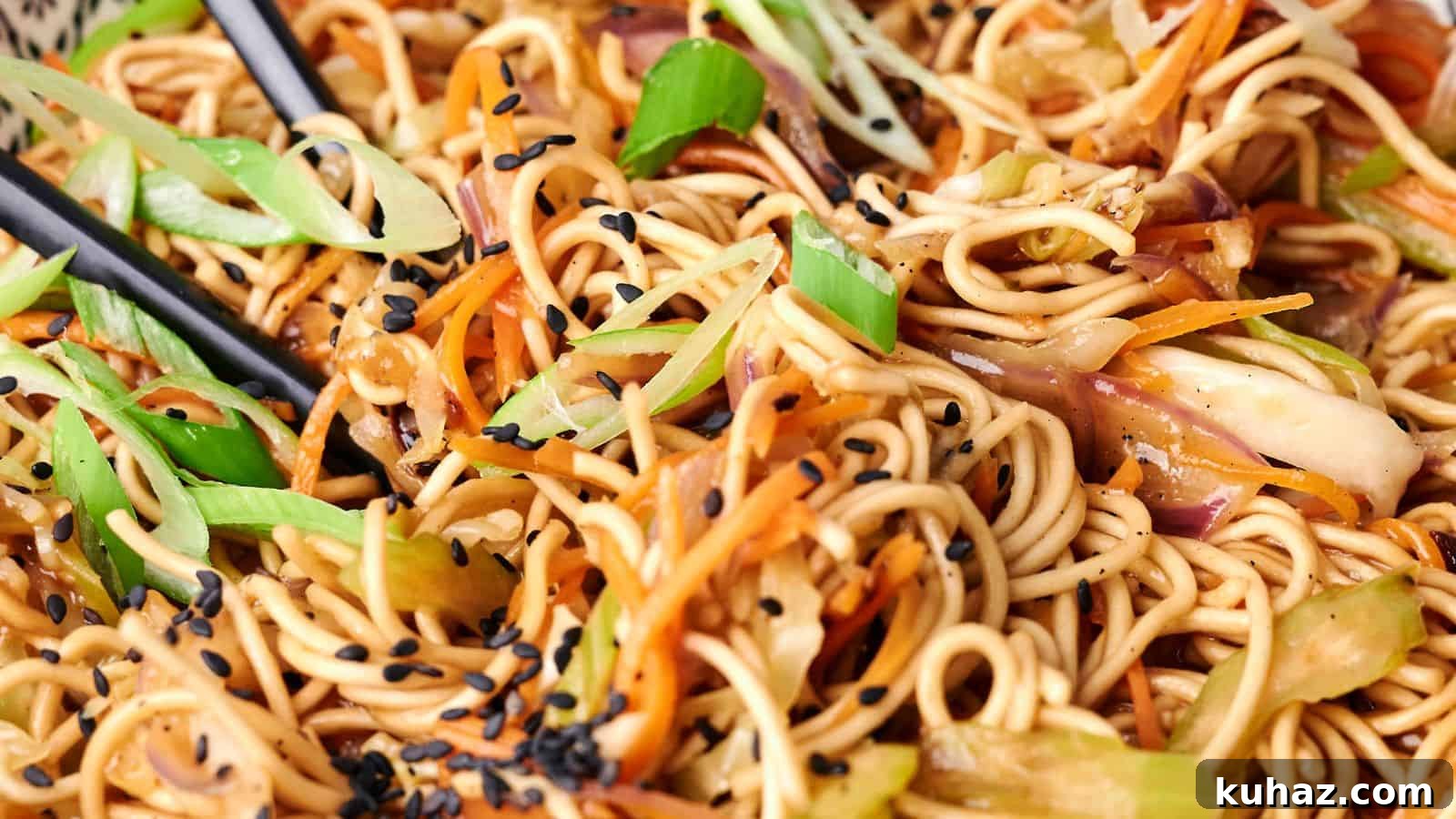 19 Asian Recipes That Fed My Family for $20 2 A close-up view of a plate of chow mein stir-fried noodles with vegetables and black sesame seeds, with chopsticks visibly picking up a portion.