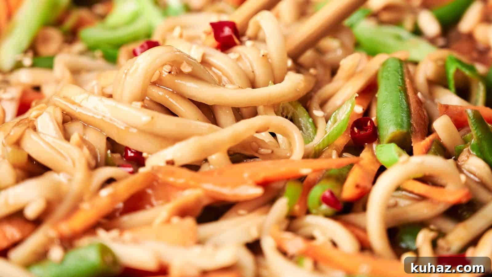 19 Asian Recipes That Fed My Family for $20 6 Close-up of stir-fried noodles with vegetables, including carrots, green beans, and chopped red peppers, garnished with sesame seeds. Chopsticks are picking up some noodles.