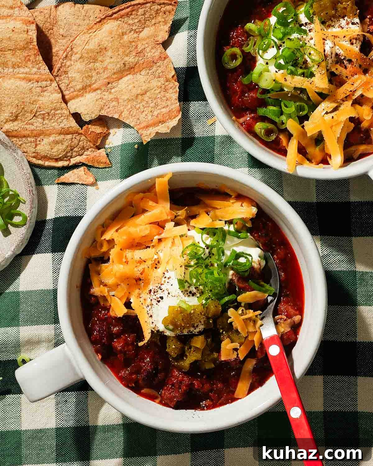 14 Crowd-Pleasing Game Day Appetizers 14 A bowl of chili topped with shredded cheese, pickled jalapeños, and green onions with an orange spoon.