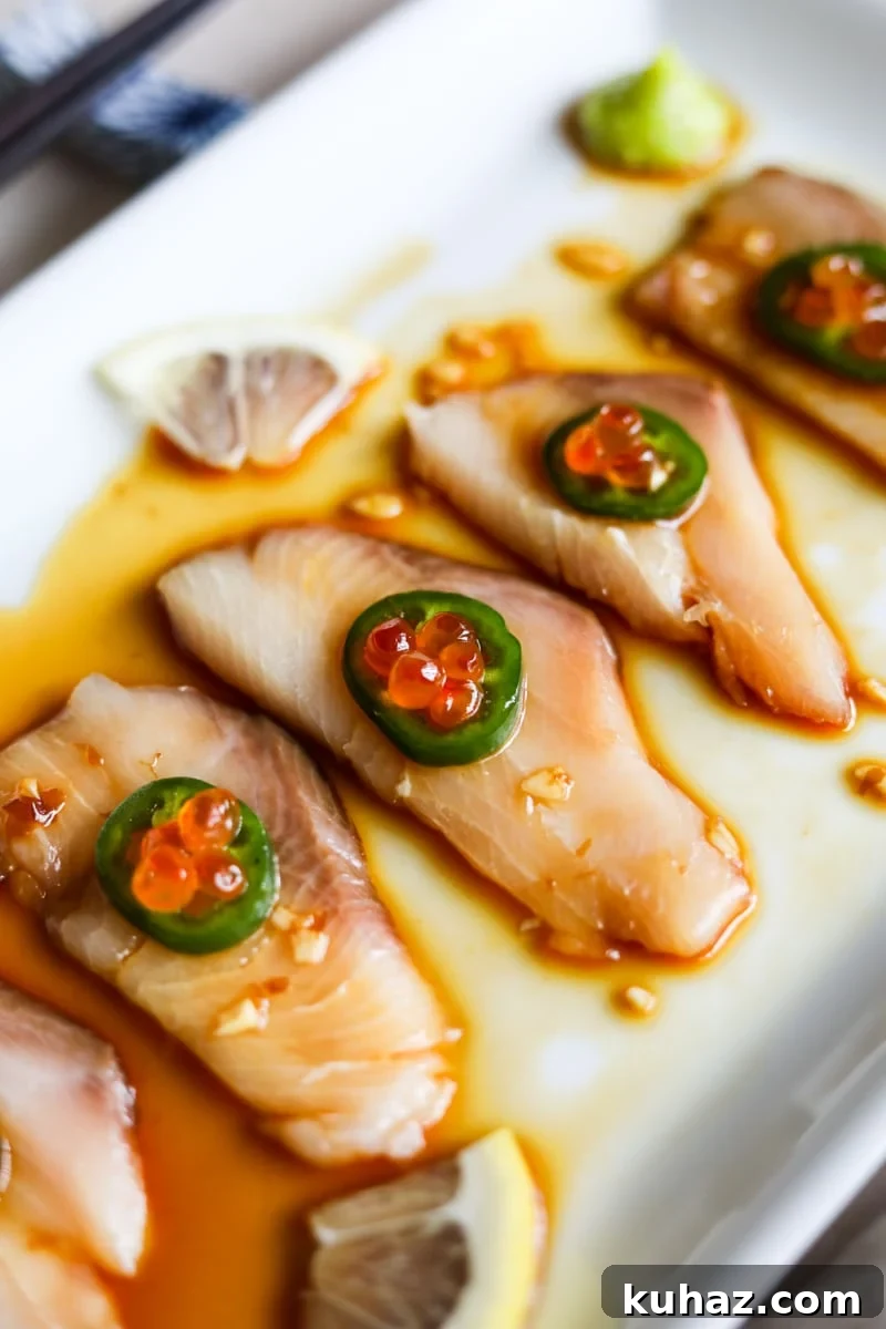 Hamachi crudo (yellowtail carpaccio) on a white plate with jalapeno, ikura, lemon, and yuzu ponzu sauce.