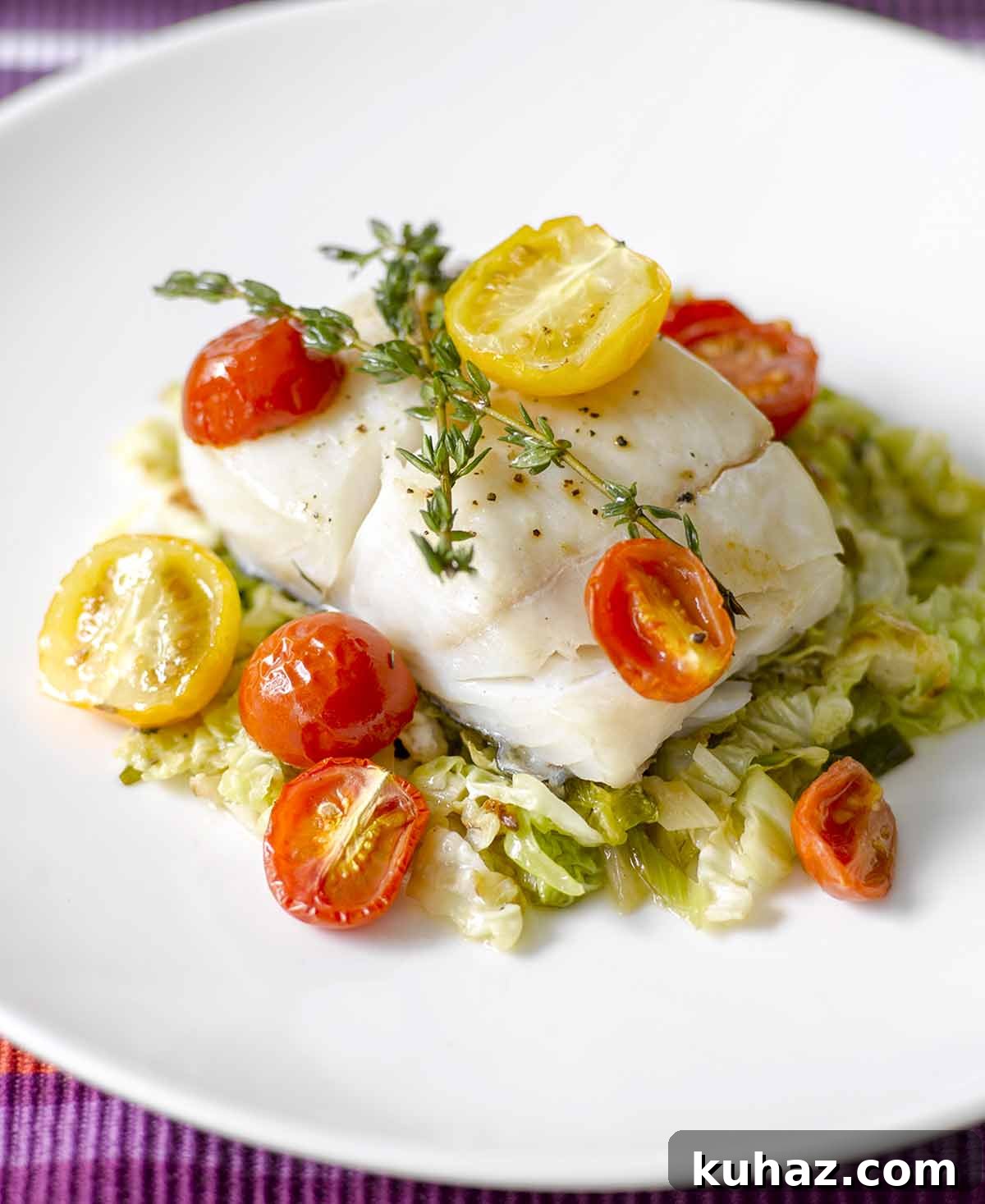 Oven-Roasted Halibut Recipe with Cherry Tomatoes and Thyme 2 A piece of oven-roasted halibut with cherry tomatoes and thyme on a bed of cooked cabbage.