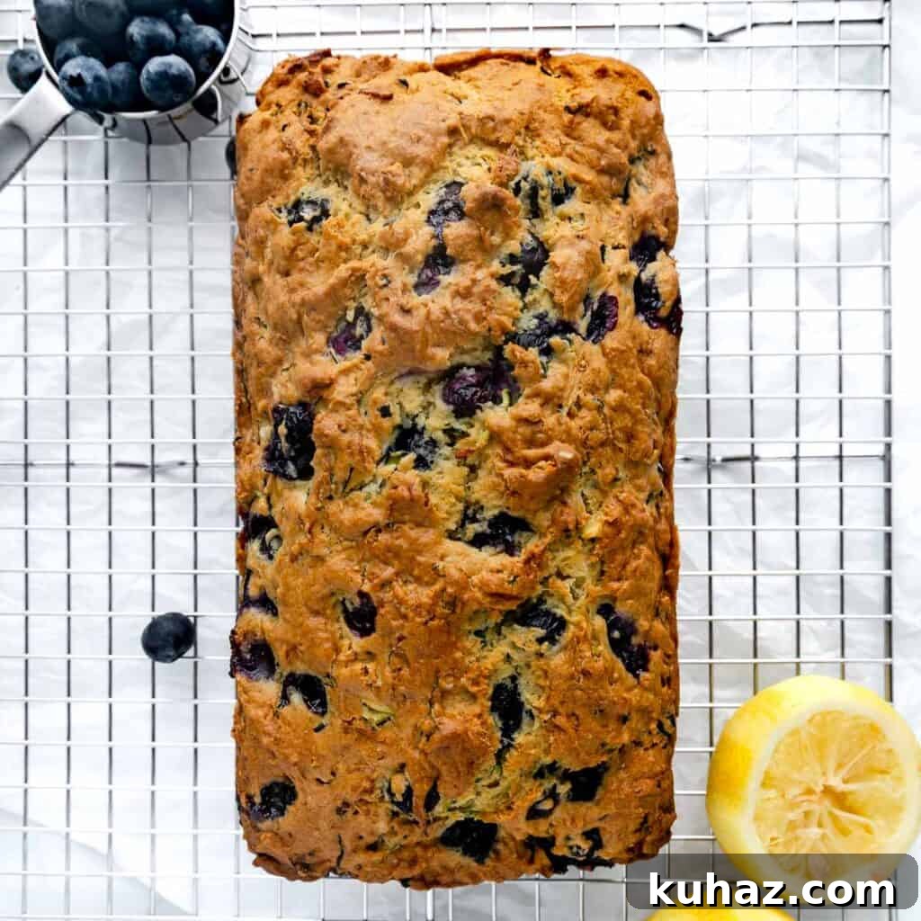 A baked loaf of bread on a cooling rack with blueberries and lemon.