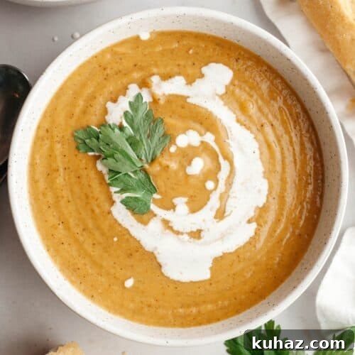 A white soup bowl with butternut squash cauliflower soup, drizzled with cream and garnished with herbs.