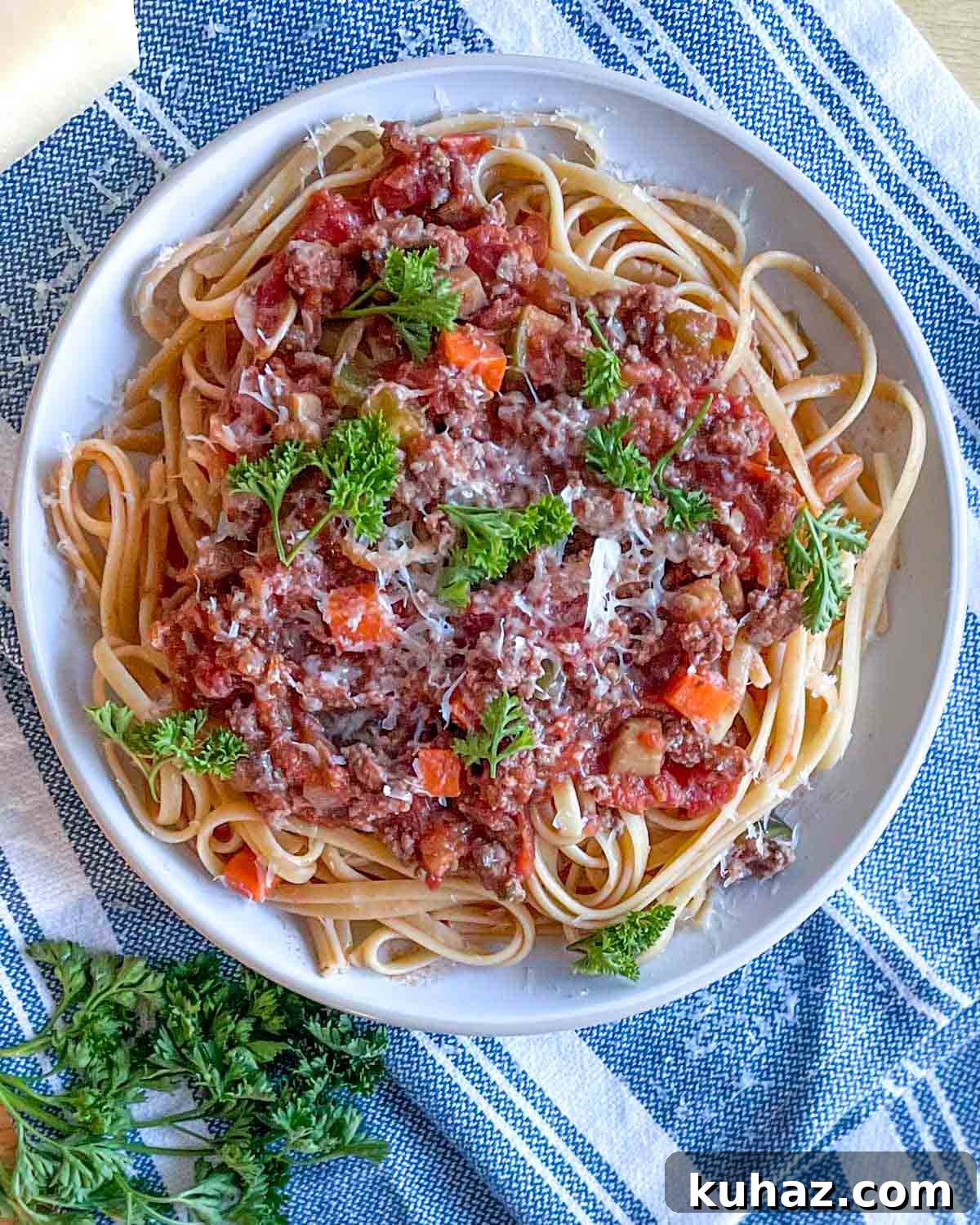 Linguine with Classic Bolognese Sauce 9 An overhead shot is shown of a dish of linguine bolognese topped with parmesan and parsley on a white and blue linen.