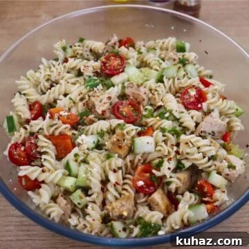 Greek chicken pasta salad in a large bowl with feta cheese and vegetables.