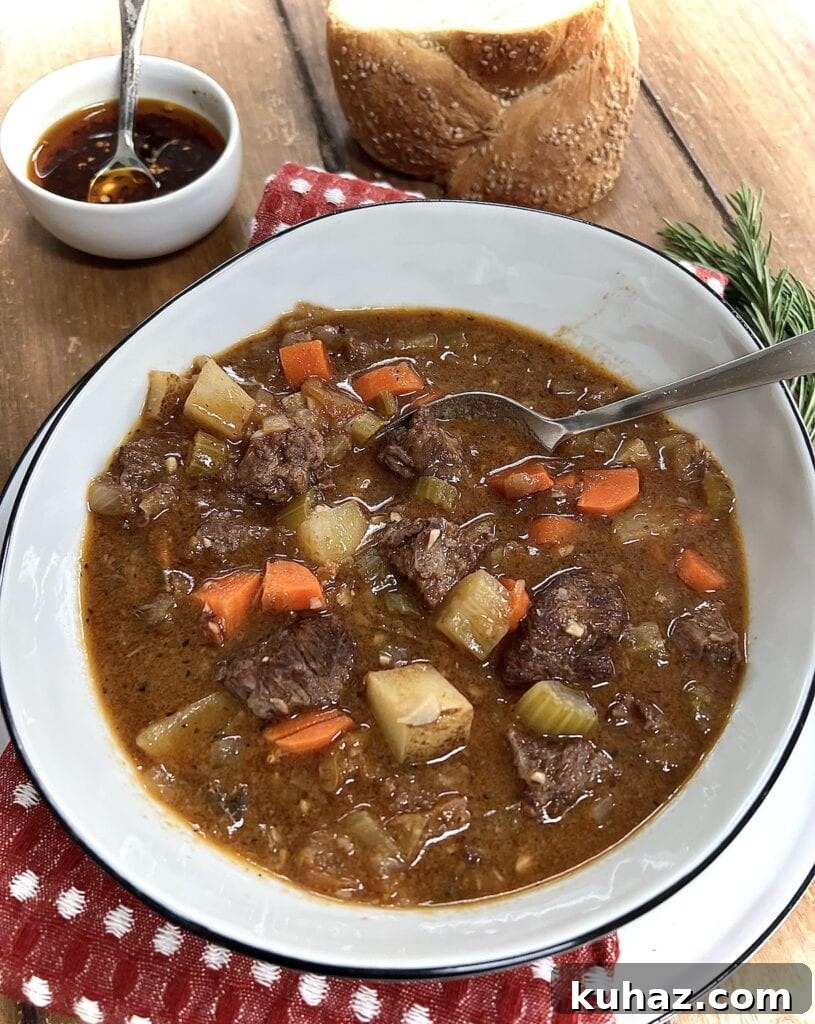Italian Beef and Potato Soup - Nonna Pot-Roast 2 Italian Beef Soup in white soup bowl with spoon and spicy oil and bread in background.