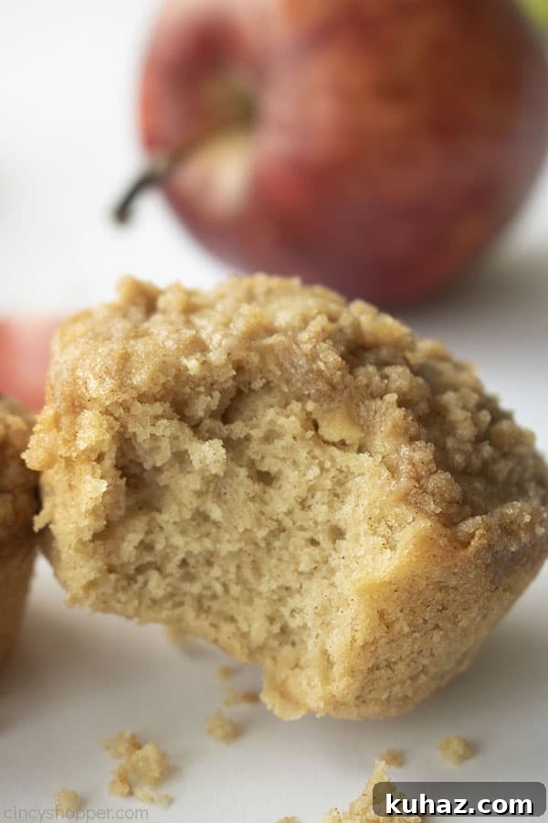 Moist Cinnamon Apple Muffins Recipe 3 Bite out of crumb muffin on a white background and red apple in the back