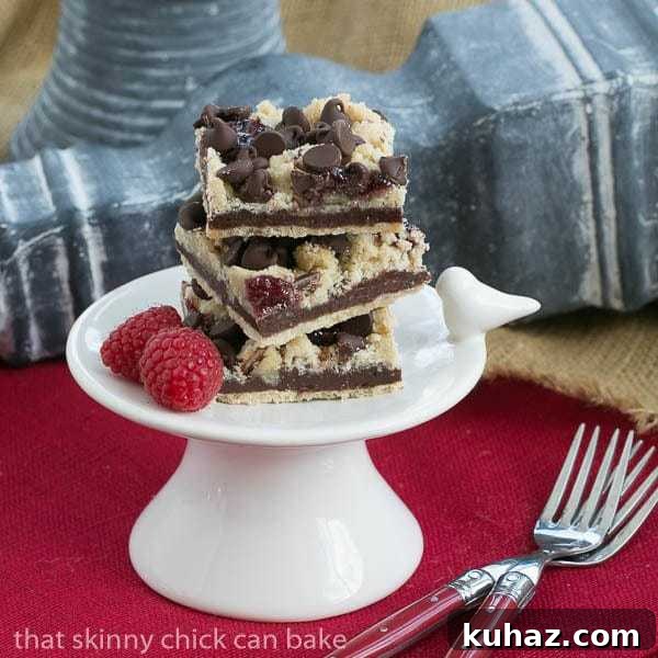 Chocolate Raspberry Crumb Bars - Shortbread, fudge, jam and a layer of crumbs makes for an out of this world bar cookie! Chocolate Raspberry Crumb Bars on a small white pedestal.