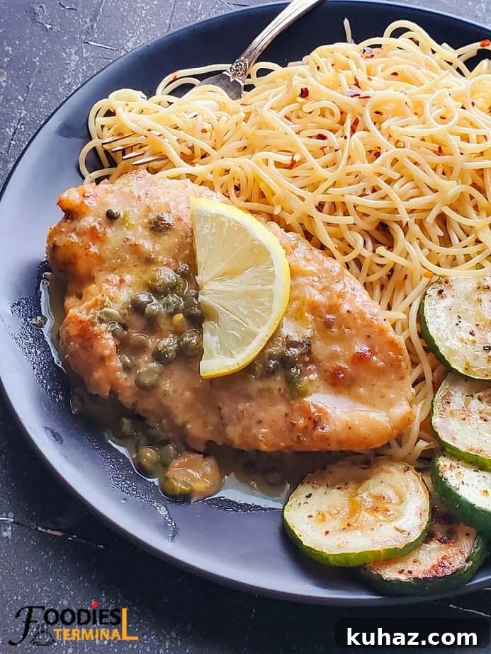 easy chicken piccata served with noodles and zucchini and a lemon wedge on a black plate