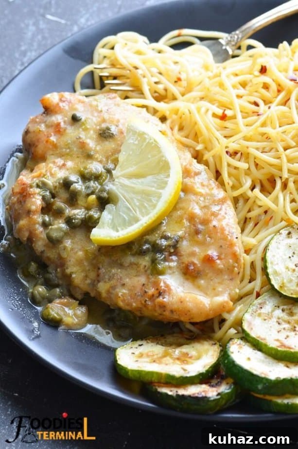 easy chicken piccata on a black plate with piccata sauce, lemon wedge, spaghetti and zucchini