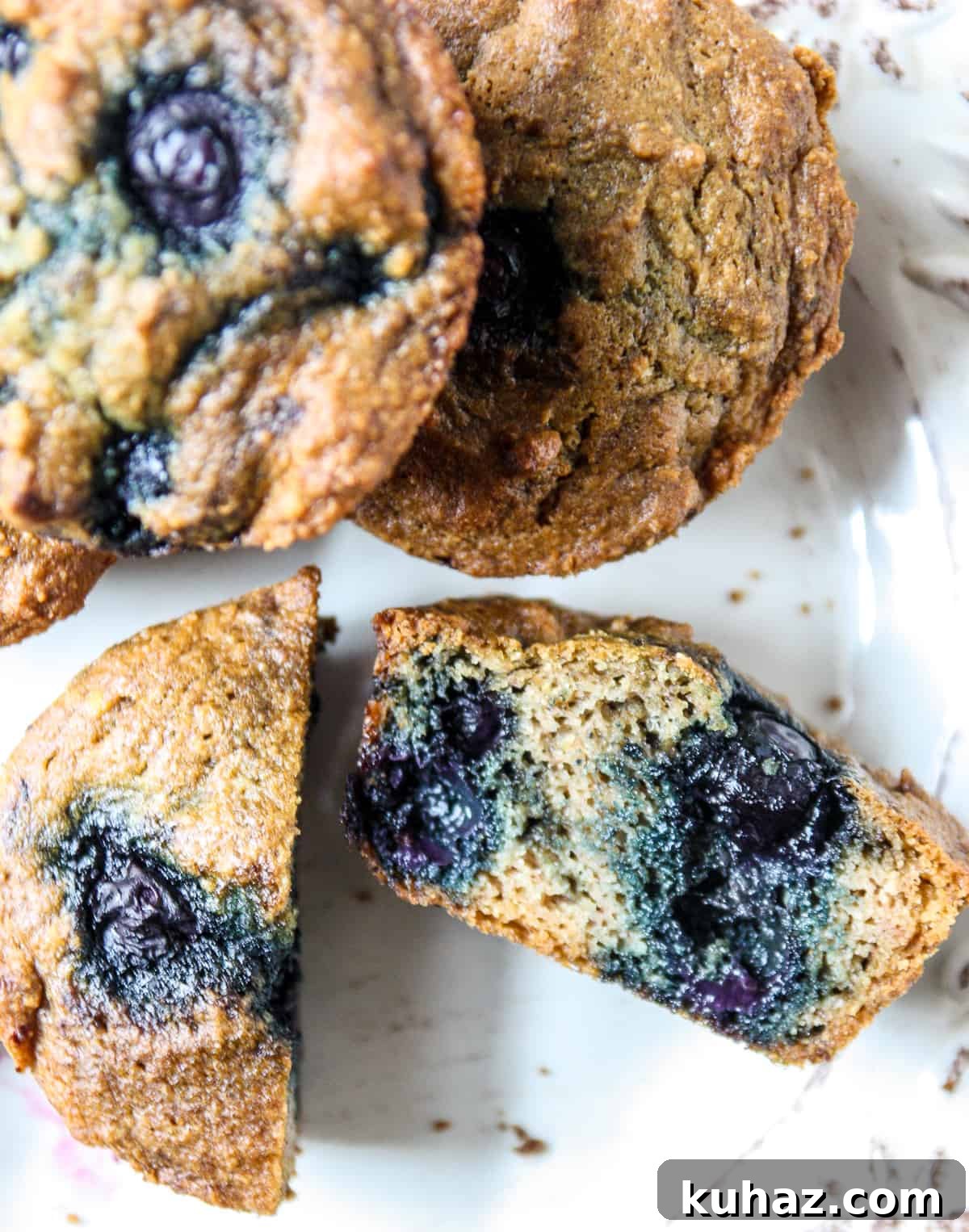 Almond Flour Blueberry Muffins, Tender and Fluffy 7 Blueberry muffins on a white plate with one of them cut in half.