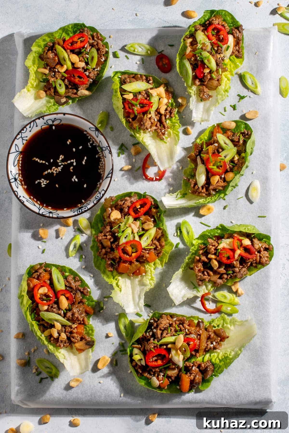 Several Yuk Sung lettuce bowl scattered across a white background with a bowl of dipping sauce. 