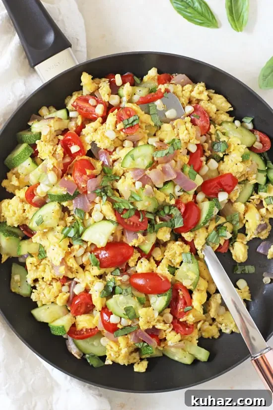 A skillet filled with Summer Veggie Egg Scramble and a serving spoon.