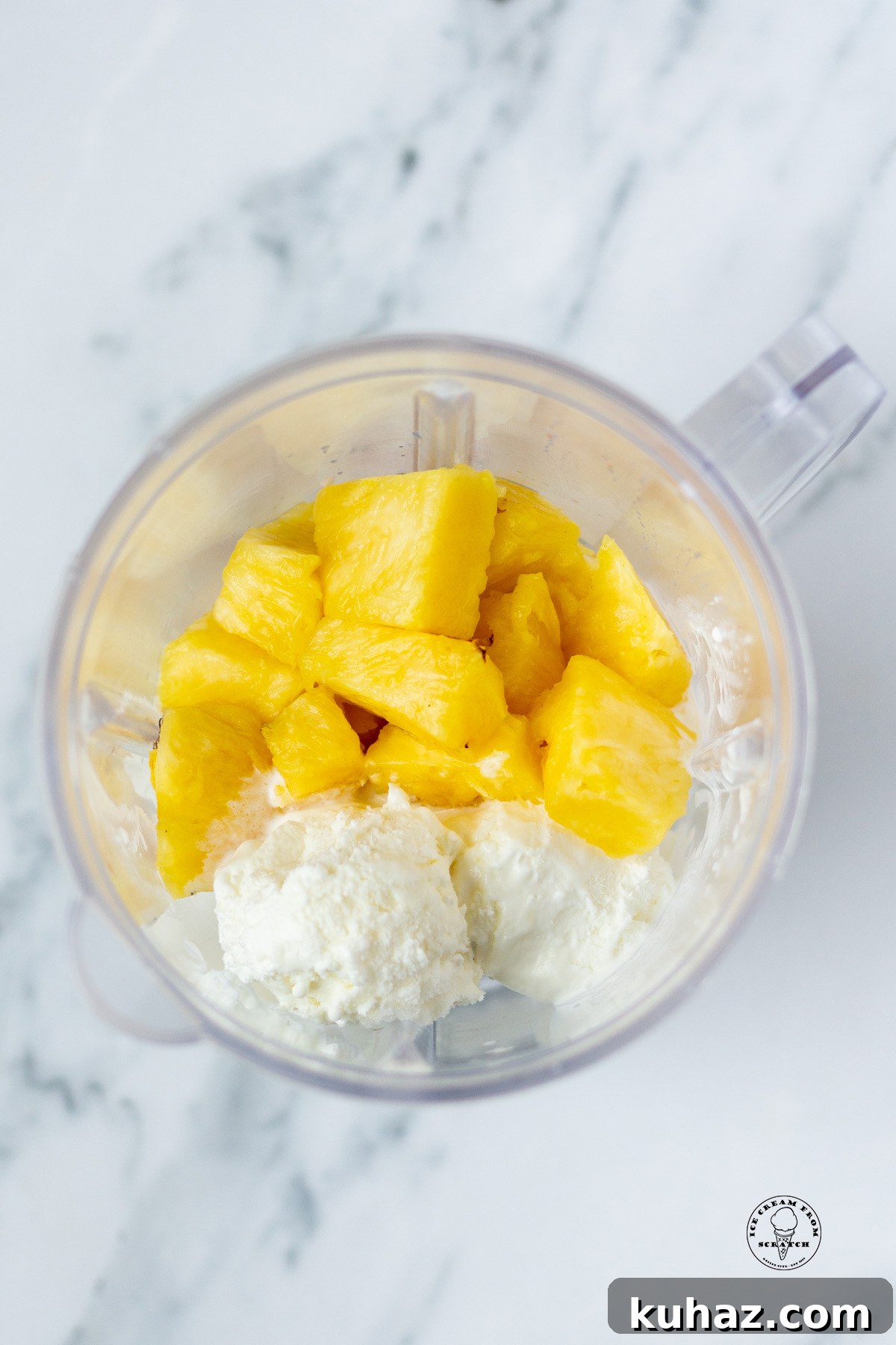 Pineapple pieces and vanilla ice cream in a blender, viewed from overhead