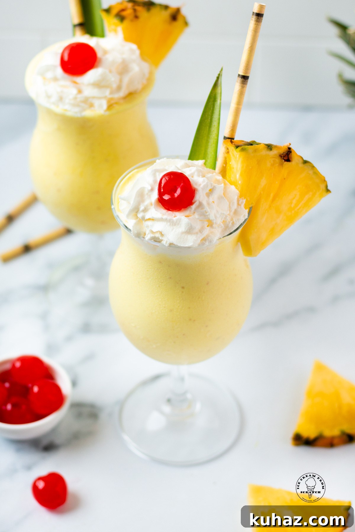 Looking down on two pineapple milkshakes garnished with cherries, pineapple slices, and bamboo straws