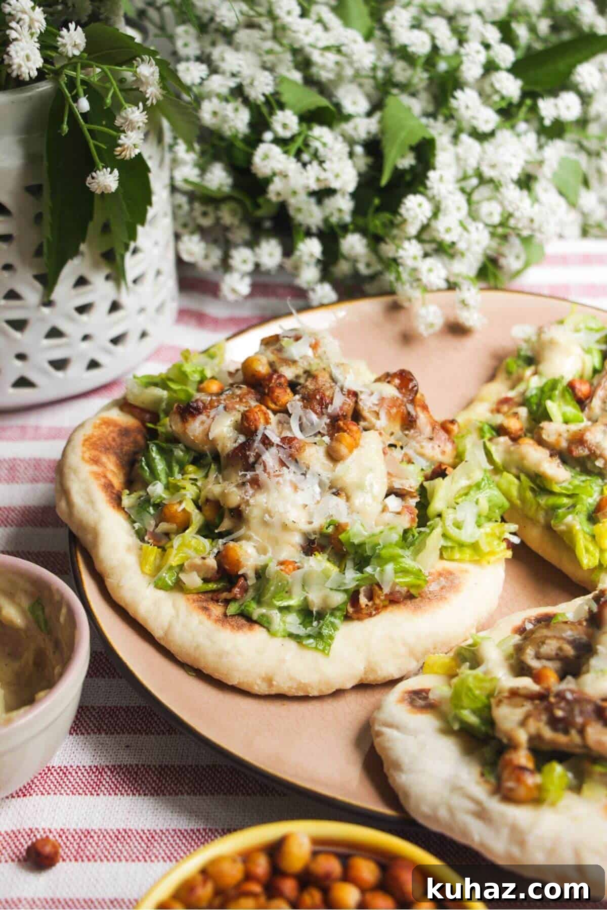 Flatbread on a plate topped with Caesar salad, charred chicken pieces and creamy Caesar dressing.