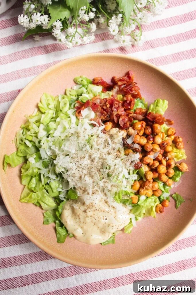 Chopped lettuce, scallions, bacon, parmesan, chickpeas and dressing in a pink bowl.