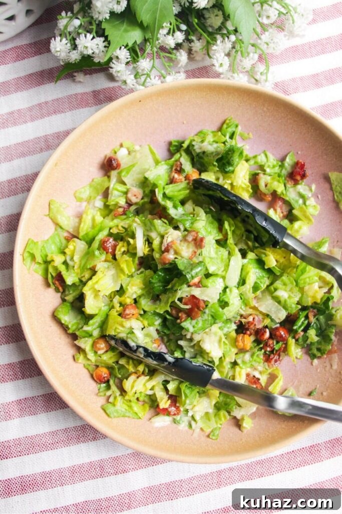 Salad mixed with tongs in a pink bowl.