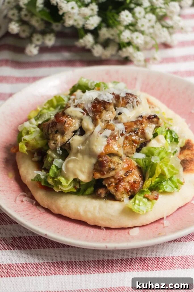 Flatbread on a plate topped with Caesar salad, charred chicken pieces and creamy Caesar dressing.
