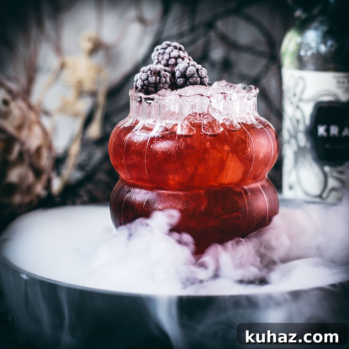 Spooky Kramble cocktail garnished with frozen blackberries on a foggy plate.