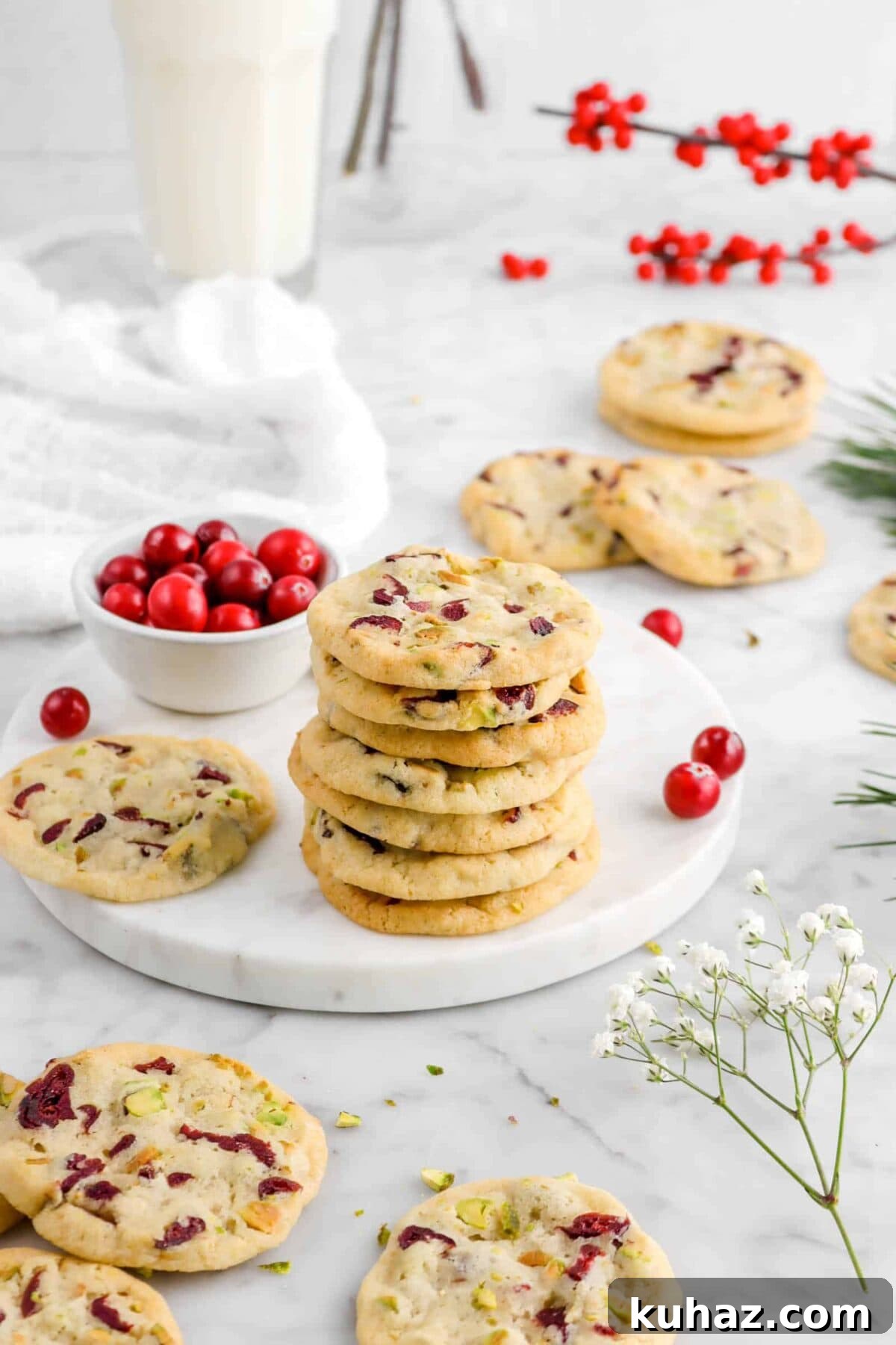 Cranberry Pistachio Slice-and-Bake Cookie Recipe 3 stacked cookies on marble plate with more cookies around, flowers, and bowl of cranberries